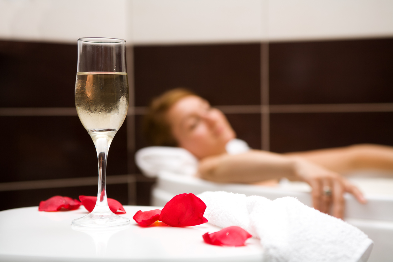 Champagne glass, roses petals and a towel in foreground and a woman relaxing in a bath tub in the background. Focus on the glass.http://www.mihaicalin.ro/p_lslb.jpg